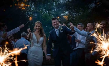 A happy bride and groom celebrate with a wedding sparkler send-off surrounded by guests outdoors at night.