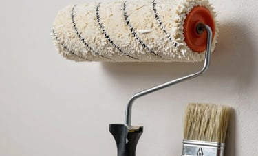 A close-up photograph of professional painting equipment, including a high-quality roller and brush with off-white paint, set against a perfectly prepped interior wall. Professional Anatolian craftsmanship, clean and reliable aesthetic.