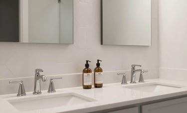 Detail shot of a contemporary dual bathroom vanity with white stone countertops and sleek light gray cabinetry. The wall features clean, white hexagonal tile work and polished modern mirrors in a North American home.