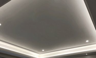 Wide angle view of a modern South American living room showing a completed drywall ceiling with recessed LED lighting and decorative molding. Sophisticated design, professional execution, charcoal and ash gray tones.