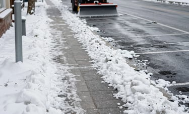 A crisp photograph of a commercial sidewalk and parking area in a Central European town, perfectly cleared of snow and salted. In the background, a small professional grit-spreading vehicle is visible. The atmosphere is cold but clean and safe.