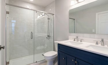 Modern master bathroom renovation in a North American / Hispanic residence. Features a walk-in glass shower, subway tiles, and a double vanity with indigo blue accents. Professional lighting highlighting clean grout lines and quality fixtures.