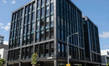 Daytime exterior shot of a contemporary office building in a commercial district of Auckland, New Zealand. The architecture features charcoal and deep teal accents.
