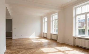 A wide-angle interior photograph of a complete home renovation in a Dutch townhouse. The space shows an open-plan living area with newly installed light oak floors, crisp white walls, and elegant ceiling moldings. Sunlight streams through large windows, showcasing a sophisticated and professional transformation of a residential space.