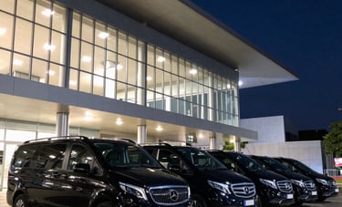A line of identical black luxury vans and sedans parked in front of a modern South American convention center at night, sophisticated urban lighting in navy and steel blue tones.