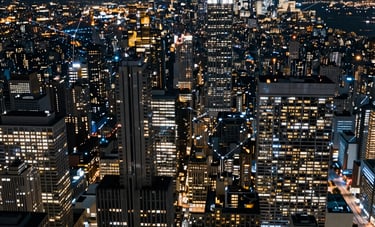 A sweeping, high-altitude nighttime photography of a North American financial district, capturing the glowing patterns of skyscrapers and city lights that represent complex network intelligence. Cool blue and steel gray tones dominate the scene.