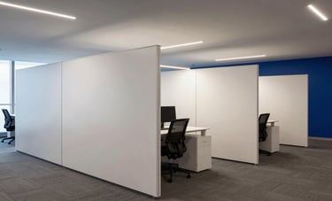 Interior of a modern commercial office in Northern Portugal. Smooth, white Pladur partition walls divide the space elegantly. Professional office lighting reflects off the clean surfaces. Neutral tones with deep blue accents. Architectural interior photography.