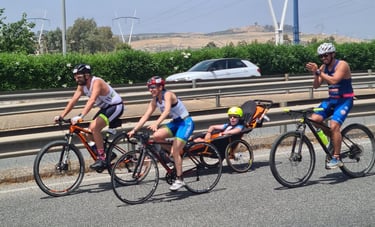 Adaptive triathlon athletes cycling on a road with a child in a racing wheelchair trailer.