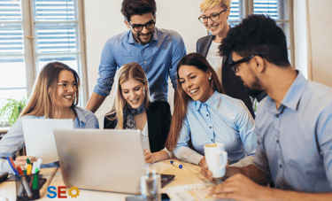 a group of people sitting around a laptop computer