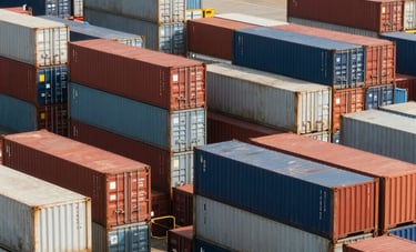 A professional photograph of a busy cargo port at daytime. Large shipping containers are stacked neatly, symbolizing global trade. International / Global Business logistics scene.