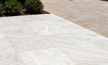 A bright, high-contrast photograph of a limestone patio and stone driveway in Austin, Texas, being meticulously cleaned. The stone looks refreshed and bright. Surrounding the stone are dark green bushes and elegant landscape lighting. The aesthetic is clean and modern.
