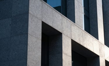 Minimalist architectural detail of a modern stone and glass structure in a North American city, conveying strength and permanence, with Slate Blue shadows and Platinum highlights.