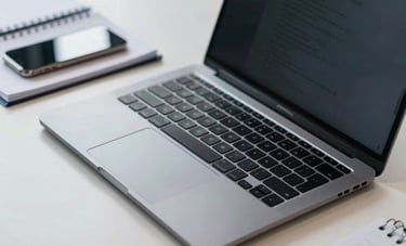 A close-up of a professional desk in an Indonesian office with a high-end laptop, a smartphone, and a notebook. The desk is organized and neat. The color scheme is steel blue and off-white, emphasizing a commitment to efficient technology and structured work systems.