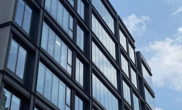 A high-end architectural photograph of a sleek, contemporary multi-story building exterior in a North American urban environment, featuring clean glass and dark navy metal accents under a bright blue sky.