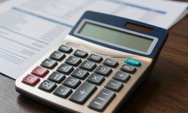 A close-up of a professional desk in a US business environment. A sleek metal calculator and neatly organized financial reports are placed on a dark wood surface. The lighting is focused and professional, highlighting the gold and navy blue tones.