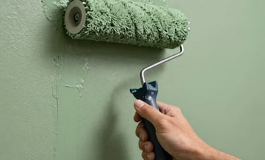 Close-up of a professional painter's hand using a roller to apply smooth sage green paint to an interior wall of a stylish Latinoamericano residence.