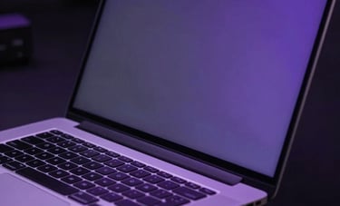 Close-up photography of a high-performance laptop screen in a dark modern environment. Soft purple glow reflects on sleek metal in a professional setting.