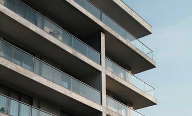 Daytime exterior shot of a contemporary South Asian residential building with glass balconies, sleek architecture, and a clear blue sky in the background.
