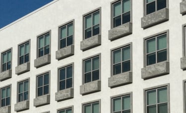 A side-view photograph of a multi-story apartment complex in Ormond Beach, Florida. Every window features consistent, solid slate-grey concrete sills. High-quality construction photography style under a clear blue sky.