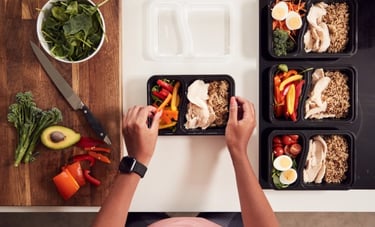 A person preparing healthy meal prep containers with chicken, brown rice, and fresh vegetables.
