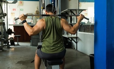 A muscular man performing lat pulldowns on a cable machine for back strength training in a gym.