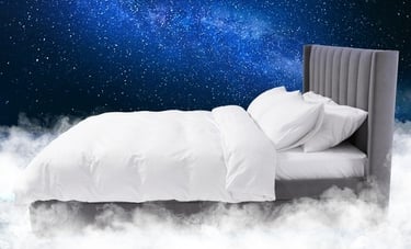 A modern grey upholstered bed with white bedding floating in white clouds under a starry blue night sky.