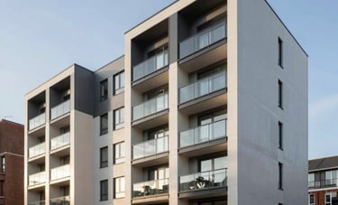 A sharp, wide-angle photograph of a modern residential development in a British suburban area. The buildings feature clean lines and contemporary glass balconies. The sky is a clear pale blue, reflecting a bright, optimistic morning. Professional architectural photography style, evoking property investment success and stability.