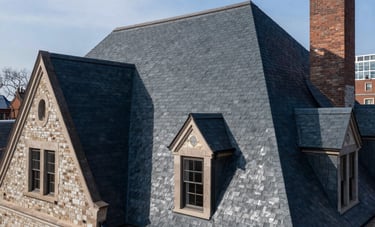 A wide-angle shot of a stately home in New York City featuring a pristine, newly installed dark navy slate roof. The architecture looks secure and durable under a clear sky, professional real estate photography style.