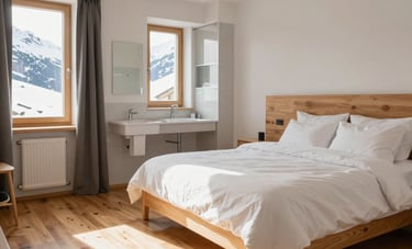 Interior of a bright Airbnb apartment in the Swiss Alps. Perfectly made bed with crisp white linens, a sparkling clean bathroom in the background, and polished wooden floors reflecting the soft sunlight. Modern and minimalist alpine decor. Central European / Swiss French style.
