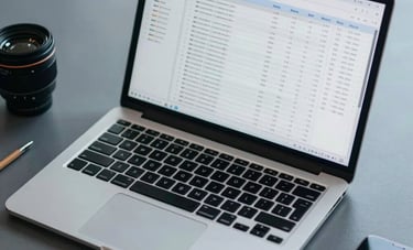 Overhead view of a laptop screen displaying complex data spreadsheets in a modern South American office. Muted blue-gray tones with professional accessories on the desk.