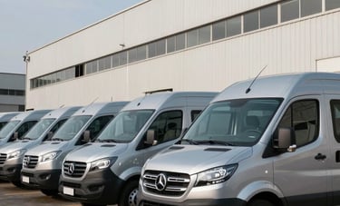 A fleet of modern, clean silver vans lined up in front of an industrial office in Brazil. The composition is sleek and highlights the scale and professionalism of the vehicle fleet under a clear sky.