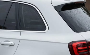 Close-up of a high-quality, custom-designed waterproof vinyl decal being applied to the rear window of a clean, modern white SUV parked in a North American driveway.