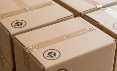 A high-angle photo of neatly stacked cardboard shipping boxes with professional circular branding stickers featuring a minimalist logo in a clean US warehouse setting.