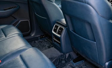 Detailed interior of a luxury vehicle in a North American / US garage, focusing on a perfectly vacuumed floor and conditioned leather seats, soft focused lighting, muted blue color palette.