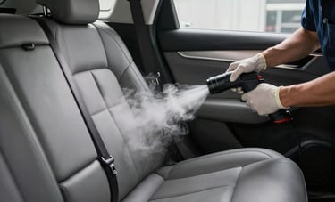 Photography of a professional technician performing steam cleaning on the upholstery of a high-end vehicle. The interior is a medium gray leather, and the steam is visible, conveying deep sanitation. Professional North American auto detailing studio environment with crisp lighting.