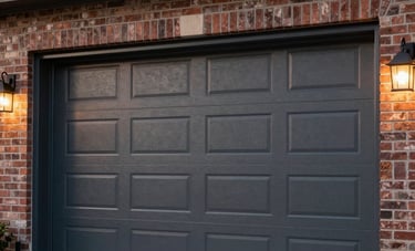 A high-end, stylish charcoal gray insulated garage door on a modern North American brick house in Orangeville. Exterior shot at dusk with warm outdoor lighting accentuating the door's clean lines and quality finish.