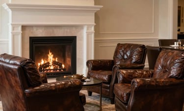 An interior shot of a luxury North American lounge with deep coffee brown leather armchairs, a warm fireplace in the background, light beige walls.