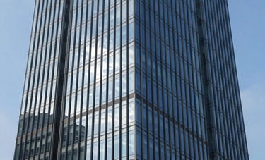 Exterior architectural shot of a modern glass-facade commercial skyscraper in Noida's business district. Blue sky reflected in the windows, clean lines, and high-end urban environment. Realistic, high-definition photography.