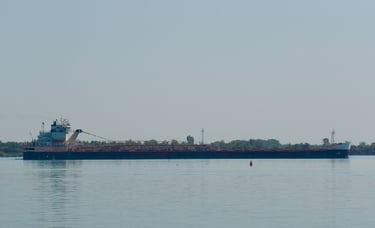 A black and white freighter passes a red buoy.