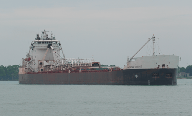A black and white lake freighter approaching, viewed from the front right.
