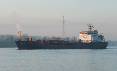 Sun shines on a blue and white tanker ship as it passes by.