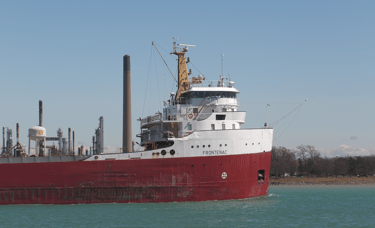 Close-up of Frontenac's red and white forward pilothouse passing an oil refinery.