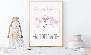 Framed wall art surrounded by a princess doll and pink accessories, with pink flowers & reads "She might be a Wildflower"