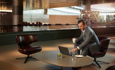 Man in suit working on laptop next to reflection pool in Qatar Airways Al Mourjan Lounge