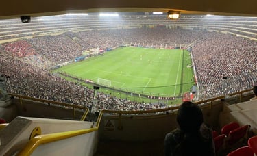Vista interna do Estádio Monumental de Lima durante uma partida, com arquibancadas amplas e gramado iluminado.