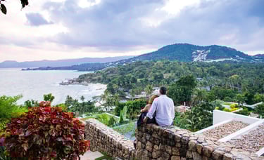A couple enjoys a romantic moment on a mountaintop overlooking Koh Samui's diverse landscape.