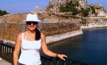 Autora diante da Fortaleza Antiga de Corfu, com a imponente estrutura histórica ao fundo.
