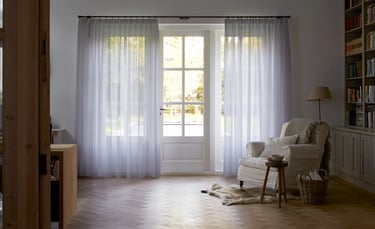 Grands rideaux tamisants blanc devant de larges fenêtres dans une entrée avec fauteuil et tapis