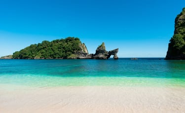 two women walking into turquoise ocean on a white sandy beach with limestone cliffs and lush green islands under blue sky