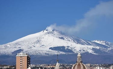 Panoramic view of snow-capped Mount Etna volcano emitting smoke above the skyline of Catania, Sicily.